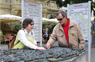 Visitante cego tateia réplica do centro antigo de Erfurt com auxílio de guia no Mercado de Peixes